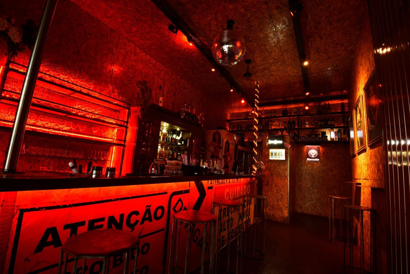 Balcão de bar revestido com placas de sinalização de trânsito, luz vermelha, prateleiras de copos e globo espelhado