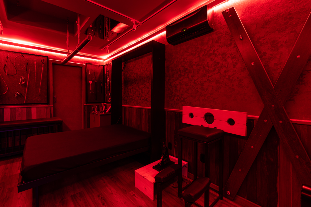 Masmorra BDSM projetada pelo Studio Inquieto em Brasília, com luz vermelha, cruz de santo andré e painéis de acessórios